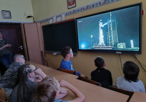 Uczniowie przed monitorem obserwują transmisję ze startu.