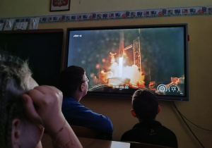 Uczniowie przed monitorem obserwują transmisję ze startu.
