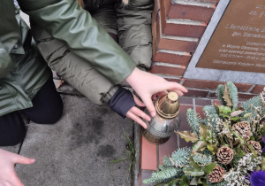 Uczniowie zapalają znicz przy grobie patrona.