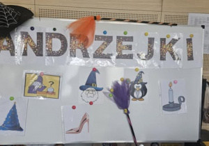 Tablica z napisem Andrzejki i i malunkami: miotły, czapki wróżki, świeczki i szklanej kuli.