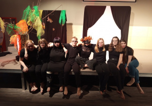 Grupa uczniów siedzi na scenie - obejmują się i uśmiechają.