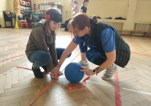Nauczycielka tłumaczy dziewczynce jak toczyć piłkę.