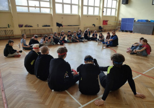 Uczniowie siedząc na parkiecie rozmawiają o sportach niewidomych.