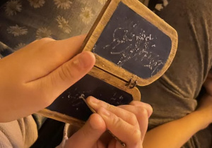 Dłonie trzymające dłutko i tabliczkę do pisania.