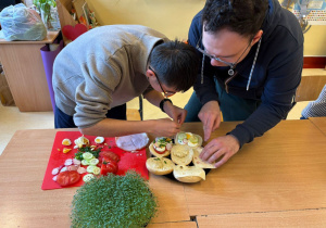 Uczniowie przygotowują bułki z wędliną i nowalijkami.