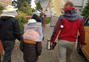 Uczniowie idą z przewodnikiem do uli.